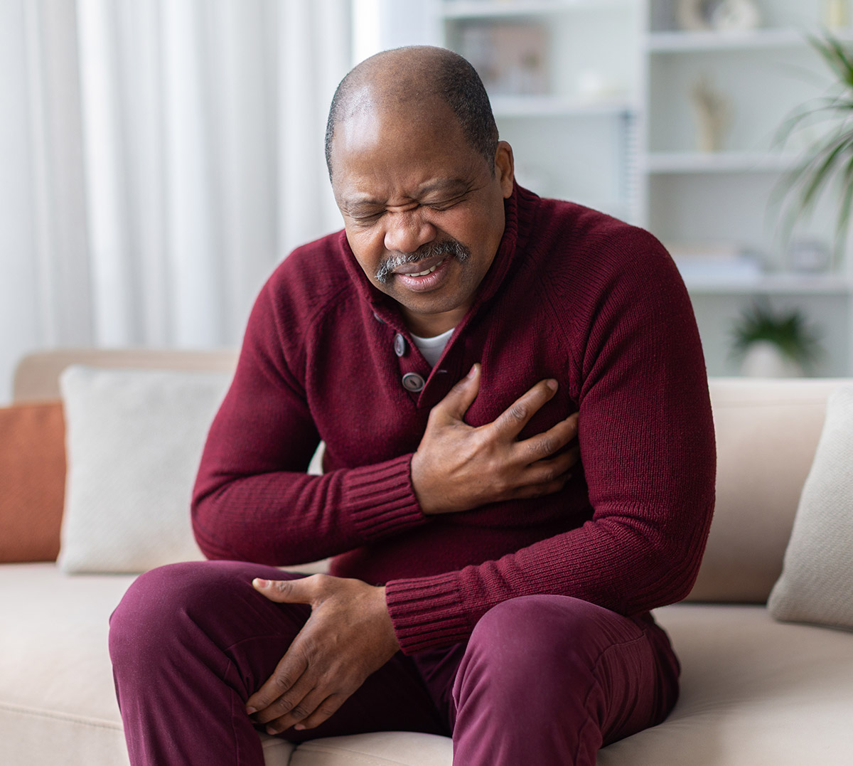 Middle aged man sitting on sofa with chest pain