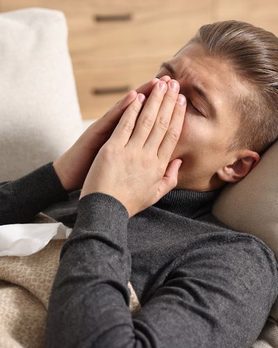 Man Sneezing Into Tissue Tucked in Hands